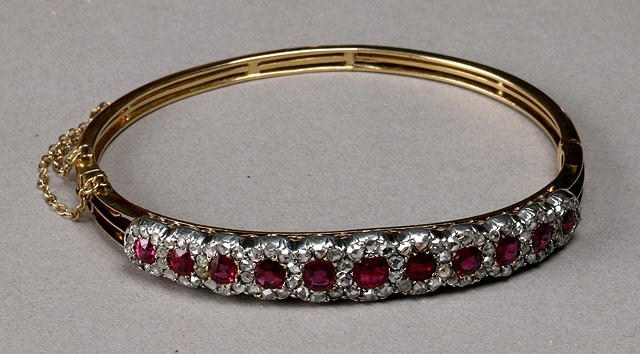 AN EDWARDIAN RUBY AND DIAMOND SET HINGED BANGLE with eleven