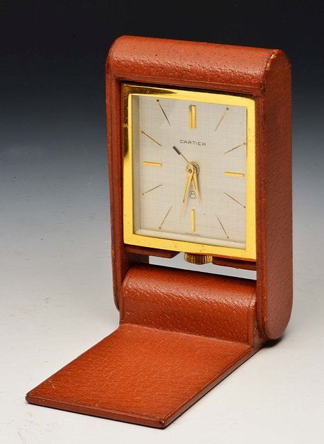 A CARTIER LACQUERED BRASS CASE TRAVELLING CLOCK in a folding