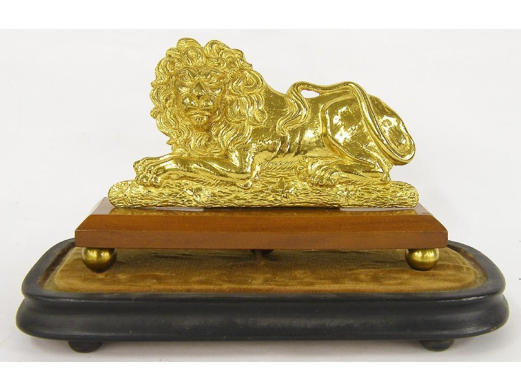Gilded metal recumbent lion upon a rectangular canted stand and