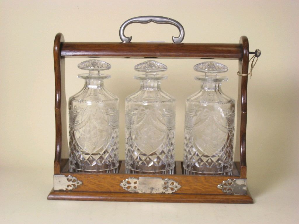 An oak plated mounted Tantalus containing three floral swag and