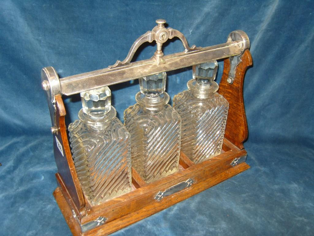 An oak and silver plated Tantalus containing three wrythen moulded
