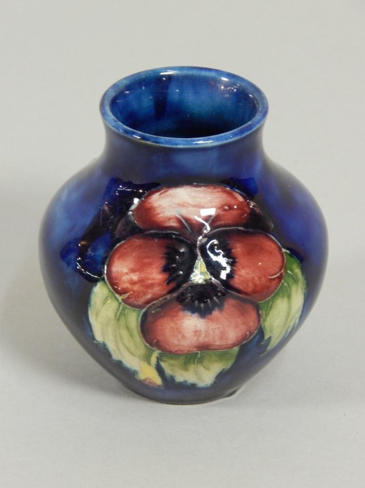 A Moorcroft bud vase decorated with pansies on a blue