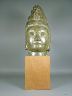 An oriental bronzed ceramic head of Guanyin on a wooden
