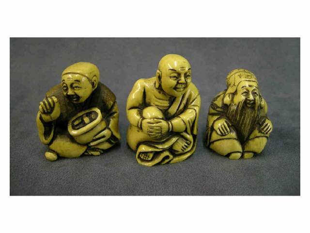 Three seated stained ivory netsuke including man sitting cross legged