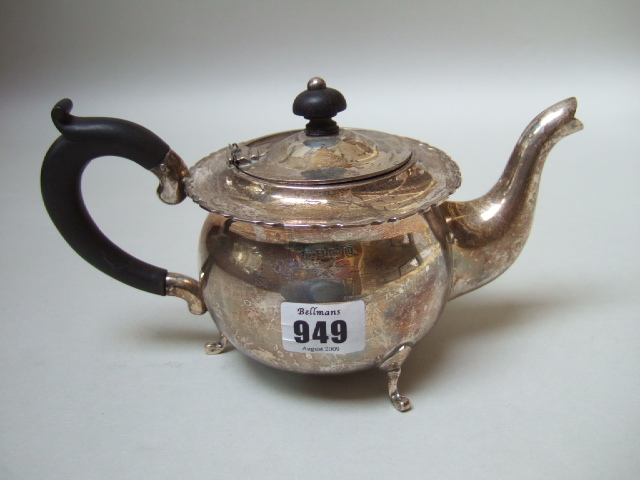 A silver teapot with a shaped rim raised on three